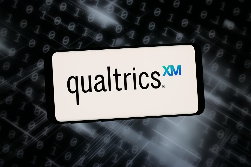 Qualtrics logo displayed on a digital screen against a background of binary code.